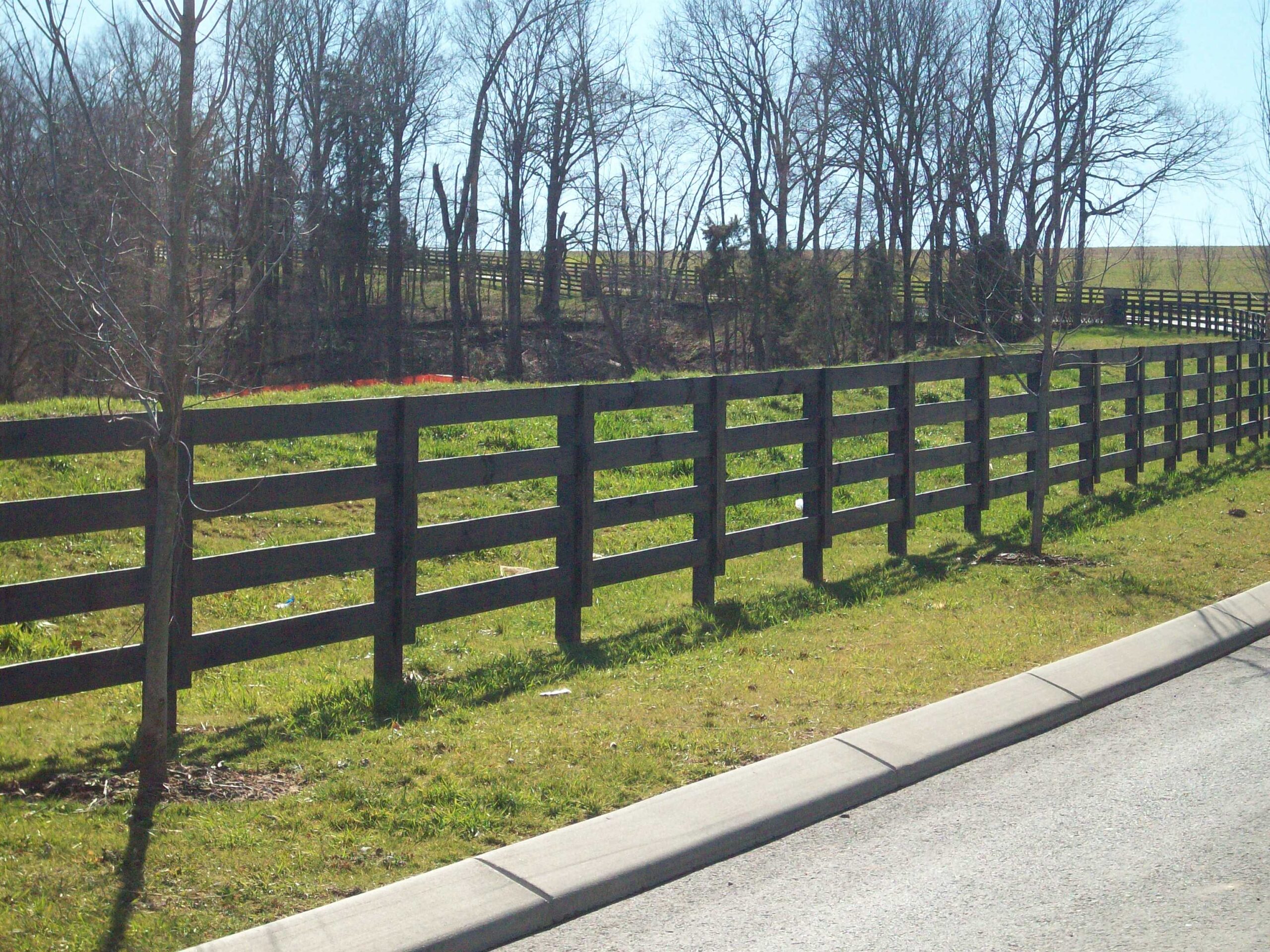 A sturdy wooden fence along a grassy field, providing both privacy and security, designed by a Nashville fence builder.